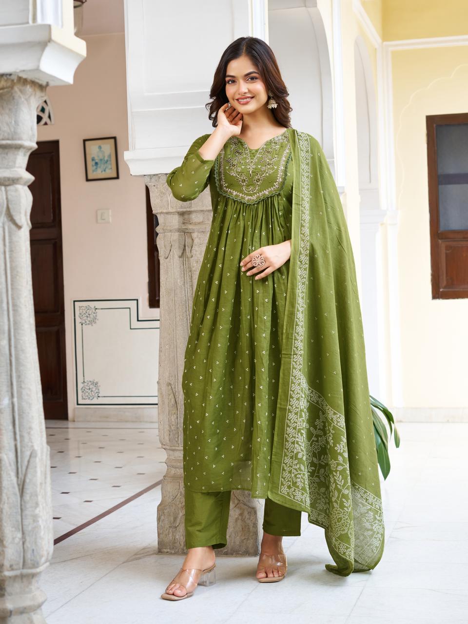 Full shot of a smiling model in an olive green embroidered cotton kurti set with matching pant and printed dupatta, posing in an arched hallway.