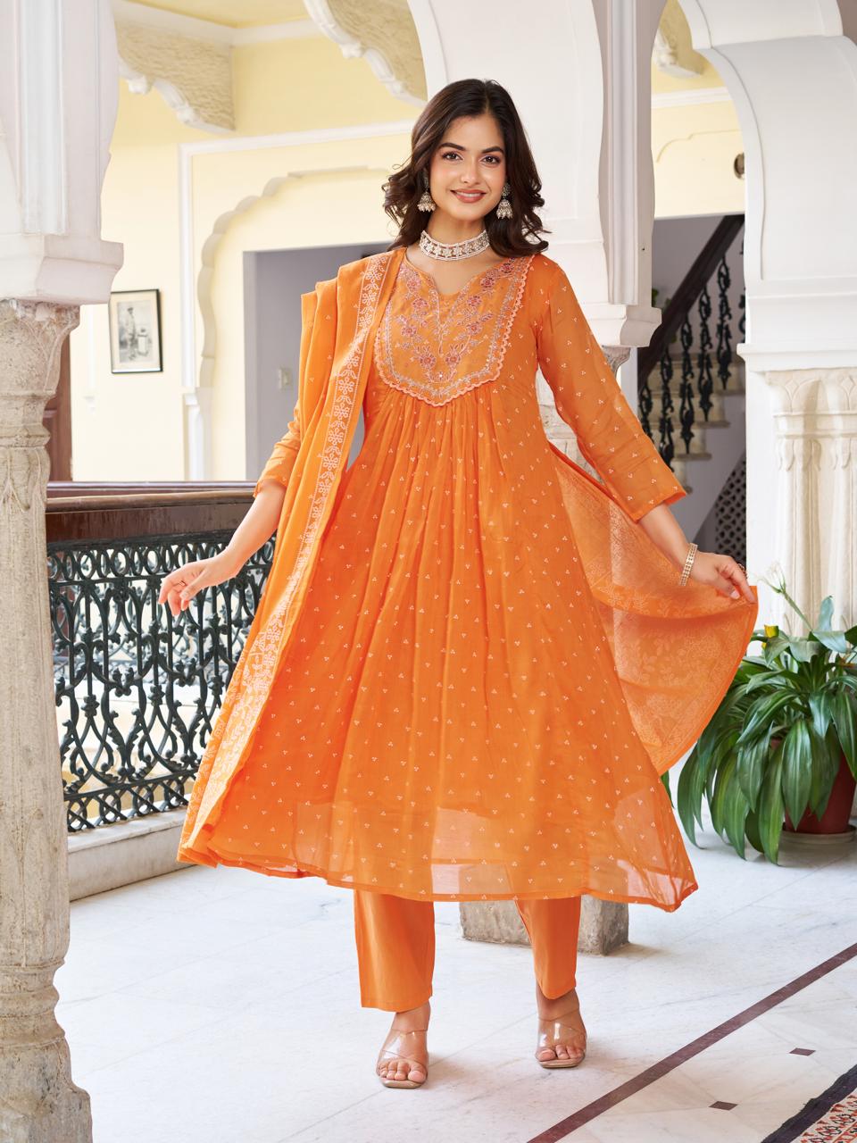 Full shot of a smiling model in a vibrant orange embroidered cotton kurti set with matching pant and printed dupatta, posing in an arched hallway.