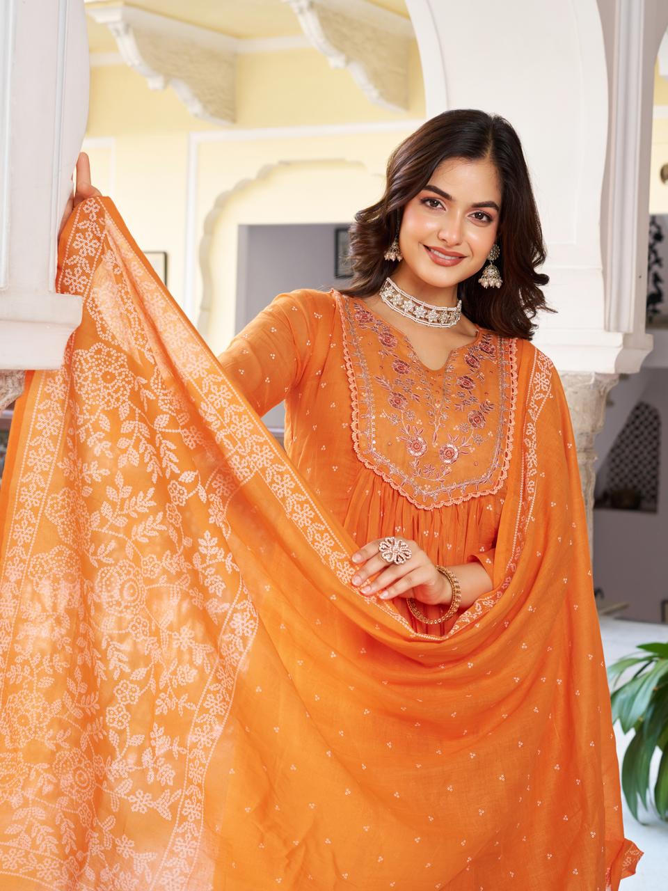 Close-up of a smiling model in an orange kurti set, gracefully holding the printed dupatta and featuring the intricate neckline embroidery.