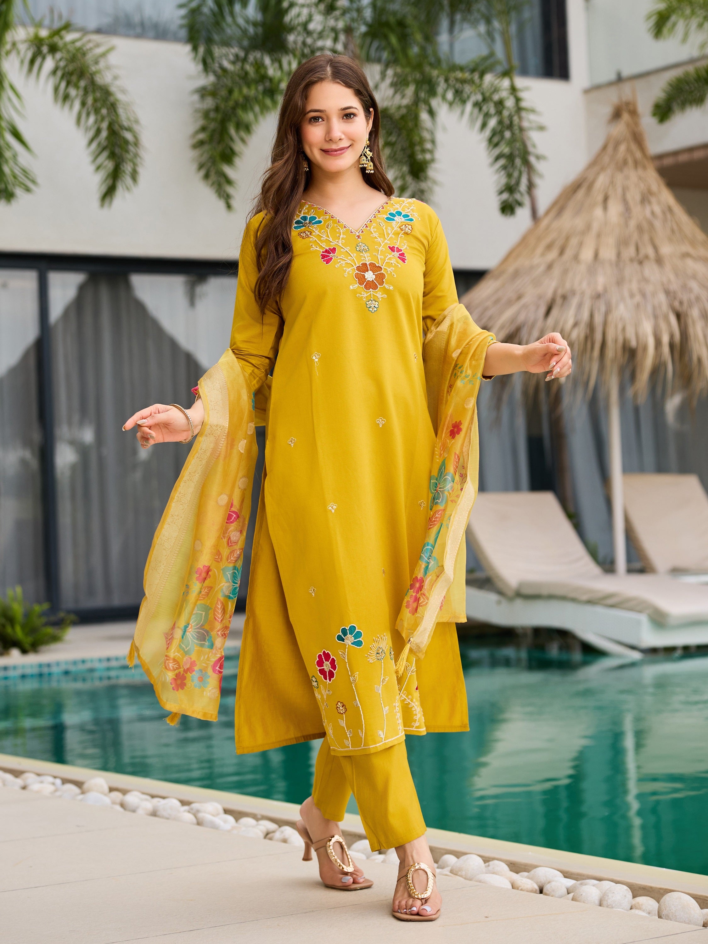 Model confidently walking and smiling in yellow embroidered kurta pant dupatta set outdoors.