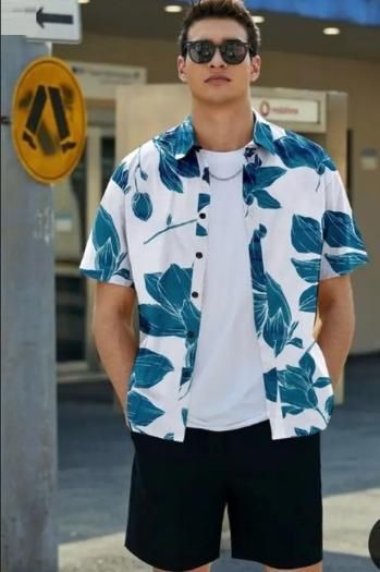 Man wearing a white shirt with blue floral pattern and black shorts outdoors.