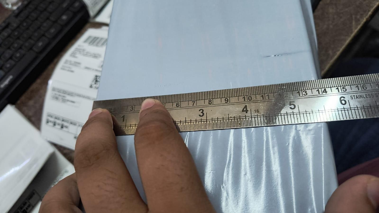 Hand holding a ruler over a white box with shipping labels.