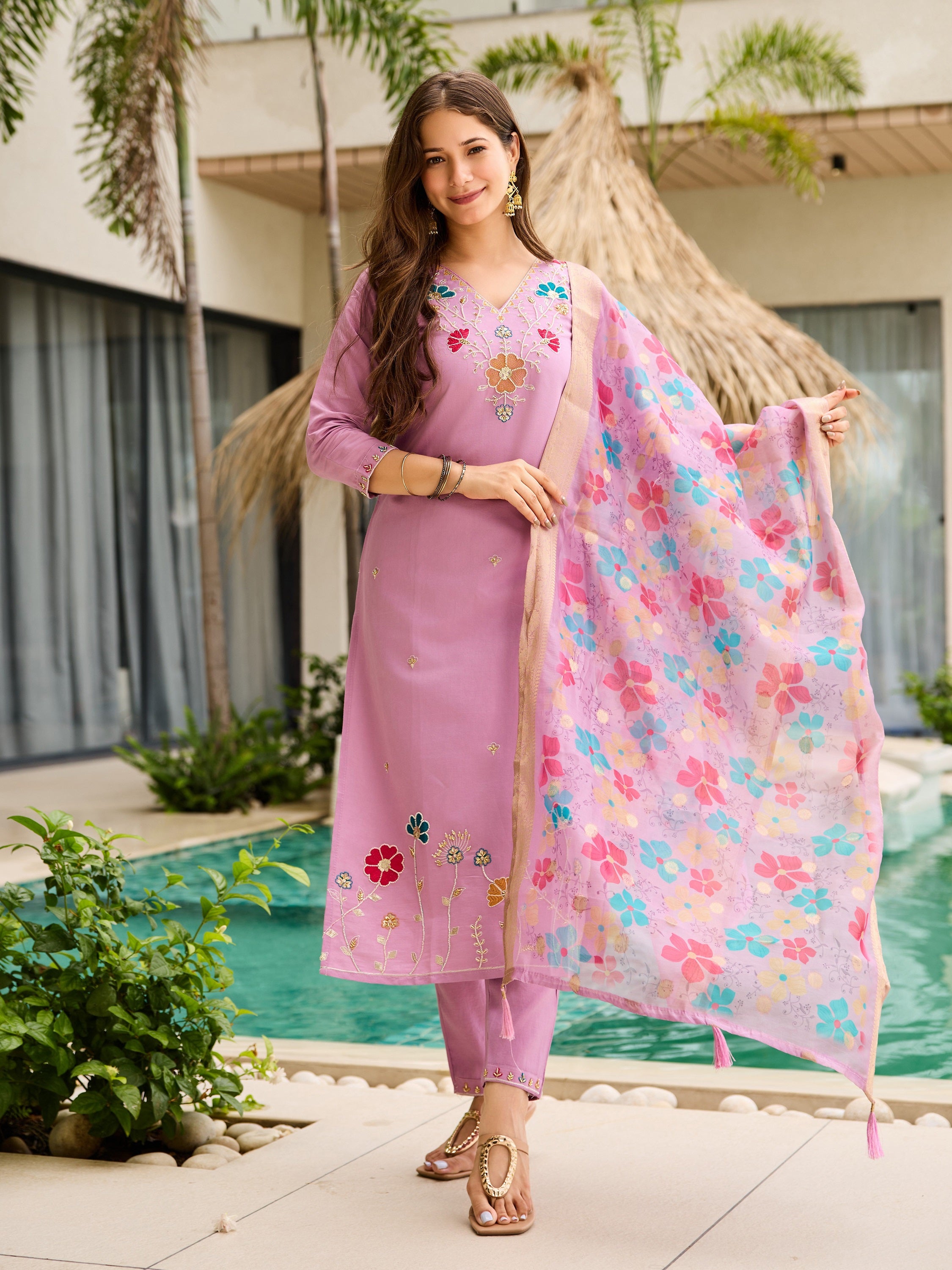 Model gracefully holding the dupatta, wearing the lavender embroidered kurta set by lush greenery.