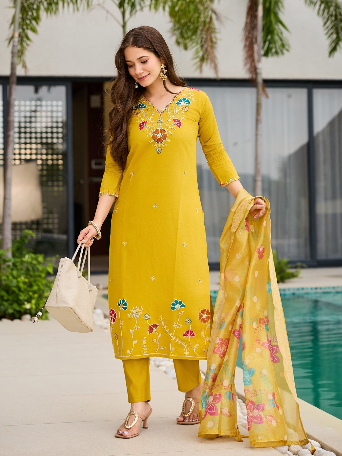 Model holding a handbag, presenting the complete yellow embroidered kurta set in an outdoor setting.