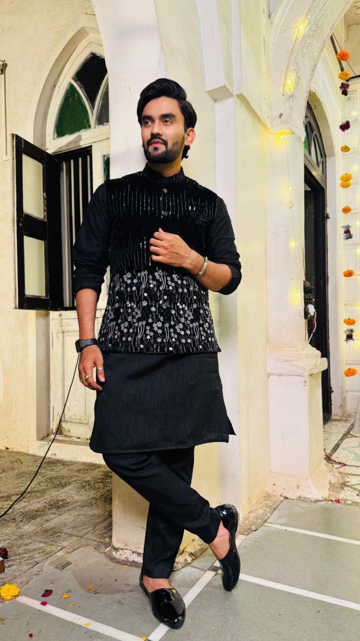 TRENDBUY Men's Black Silk Kurta Pyjama with embellished velvet coti, striking a pose in a traditional setting.