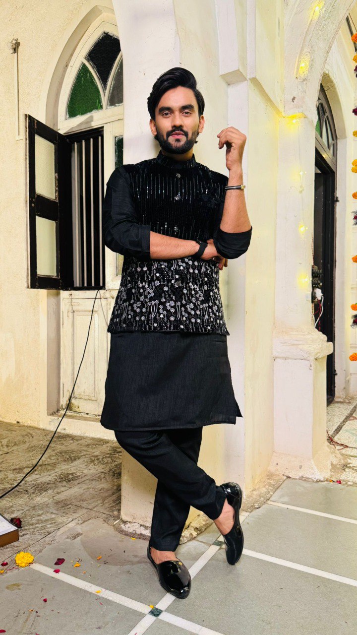 Man in black traditional outfit posing in front of a building entrance.