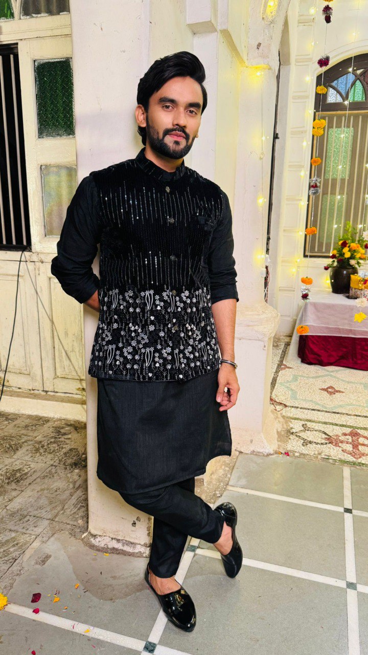 Man in traditional black outfit standing in a decorated indoor setting