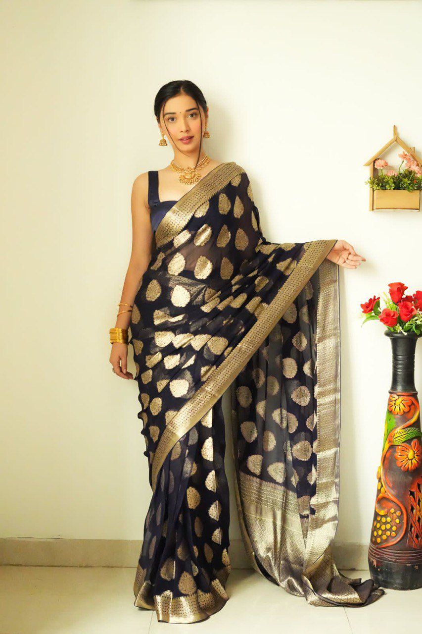 TRENDBUY model showcasing an elegant navy blue ready-to-wear saree with golden zari polka dots and broad golden border, posing gracefully against a white wall.