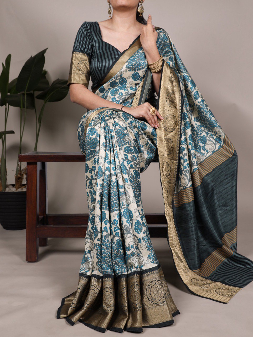 TRENDBUY model elegantly draped in a sky blue printed Tasar silk saree with a shimmering viscose border, seated on a stool.