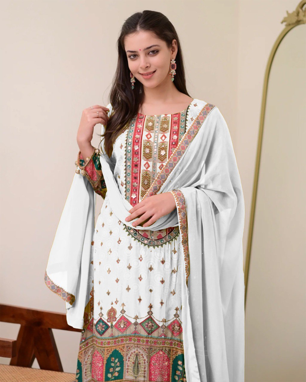 Portrait of model smiling in Ivory Pakistani suit, highlighting the detailed neckline, sparkling mirror work, and matching earrings.