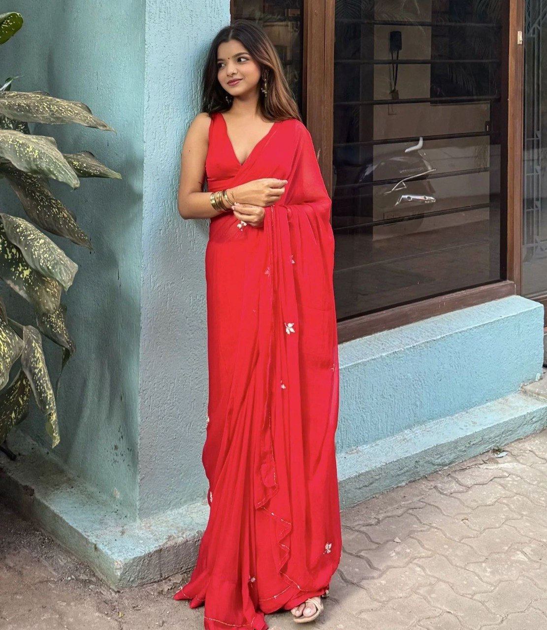 Stylish model standing elegantly in a red georgette saree, highlighting its subtle shimmer and design.