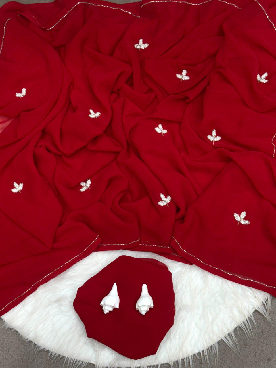 Overhead shot of a rich red georgette saree with sparkling silver cut dana leaf embroidery and a fine border.