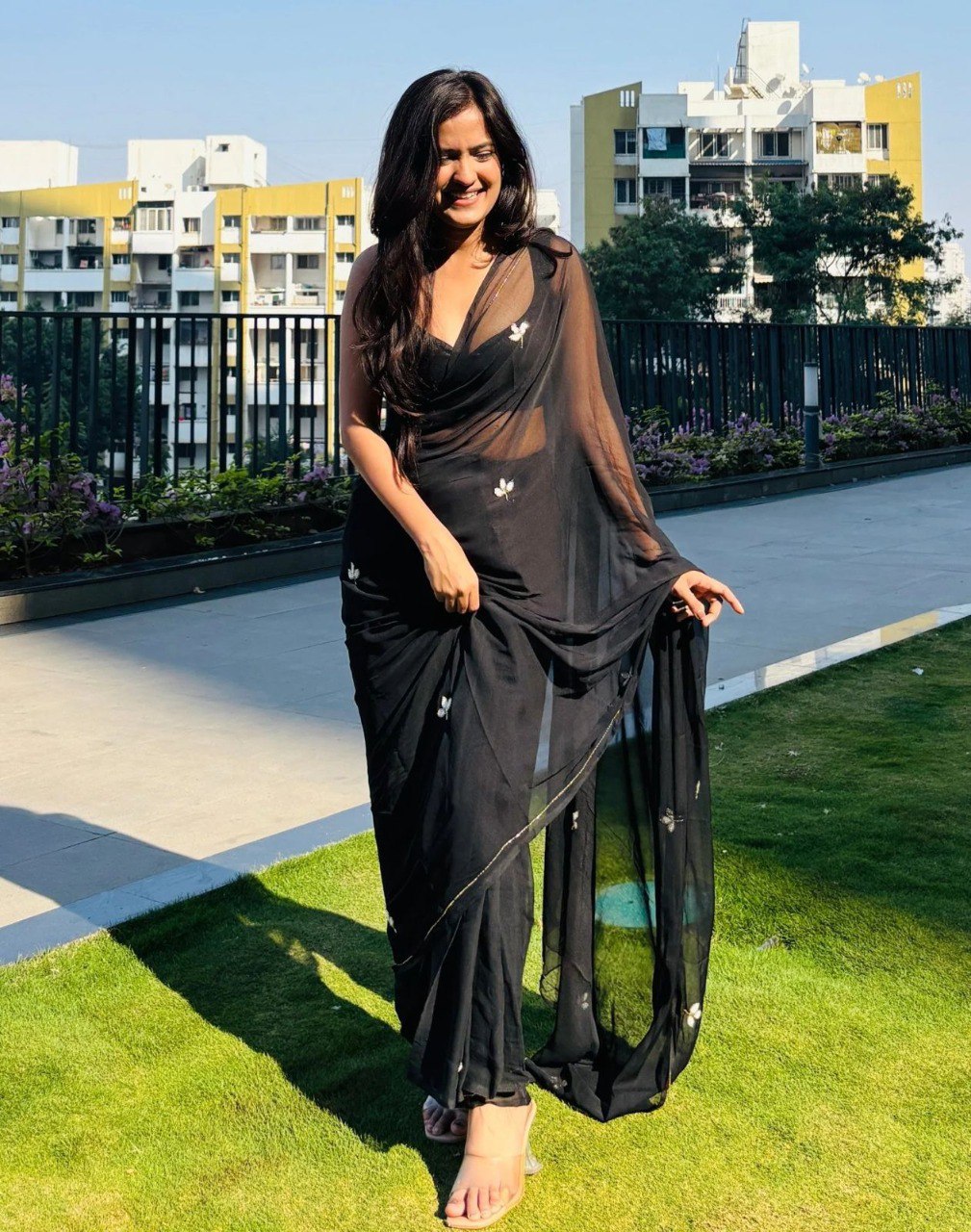 Model enjoying a sunny day, wearing a beautiful black georgette saree with delicate leaf cut dana details.