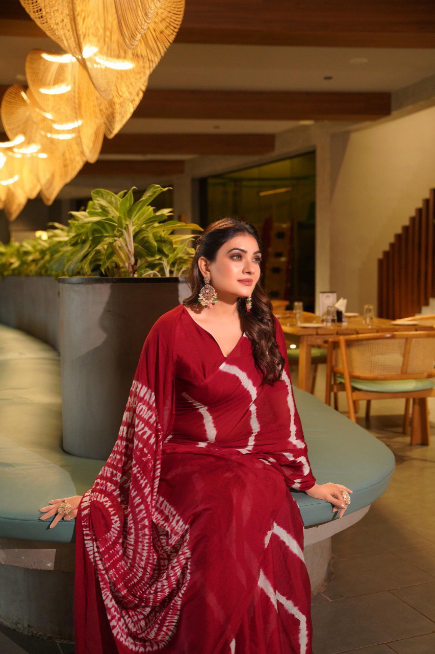 TRENDBUY model seated, featuring a deep maroon Pure Chinoon Hand Shibori Laheriya saree with bold patterns.