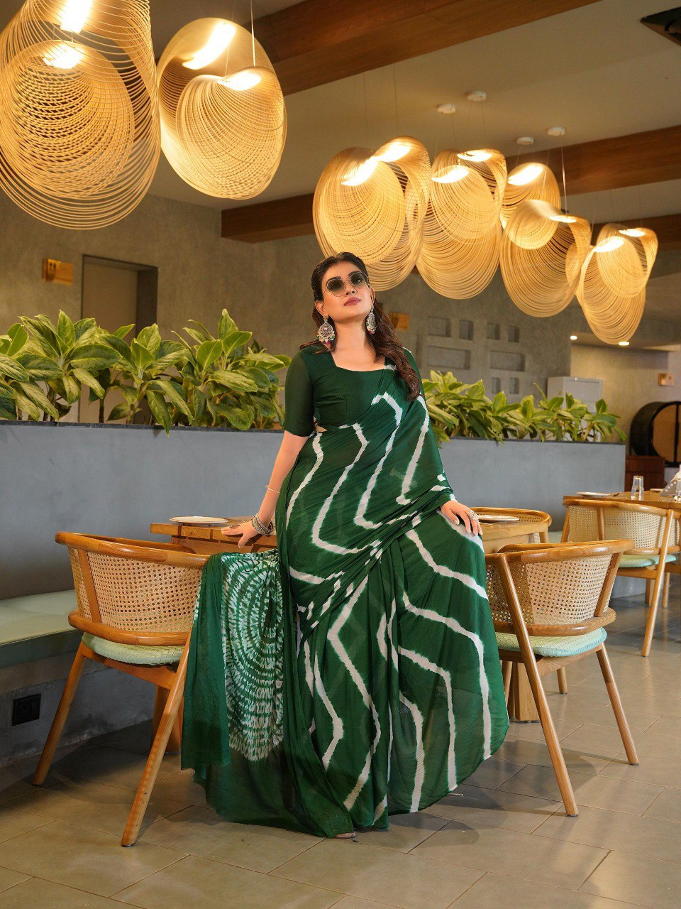 TRENDBUY model seated, wearing a sophisticated dark emerald green Pure Chinoon Hand Shibori Laheriya saree.