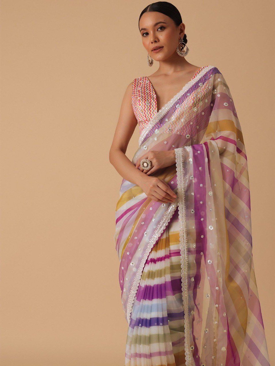 Model posing elegantly in a pink and yellow striped georgette saree with intricate details and a matching blouse.