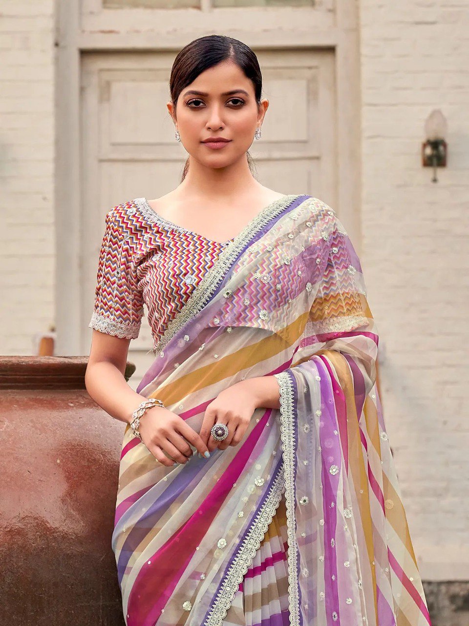 Model in pink and yellow striped saree, posing outdoors with elegant posture, highlighting design and color.