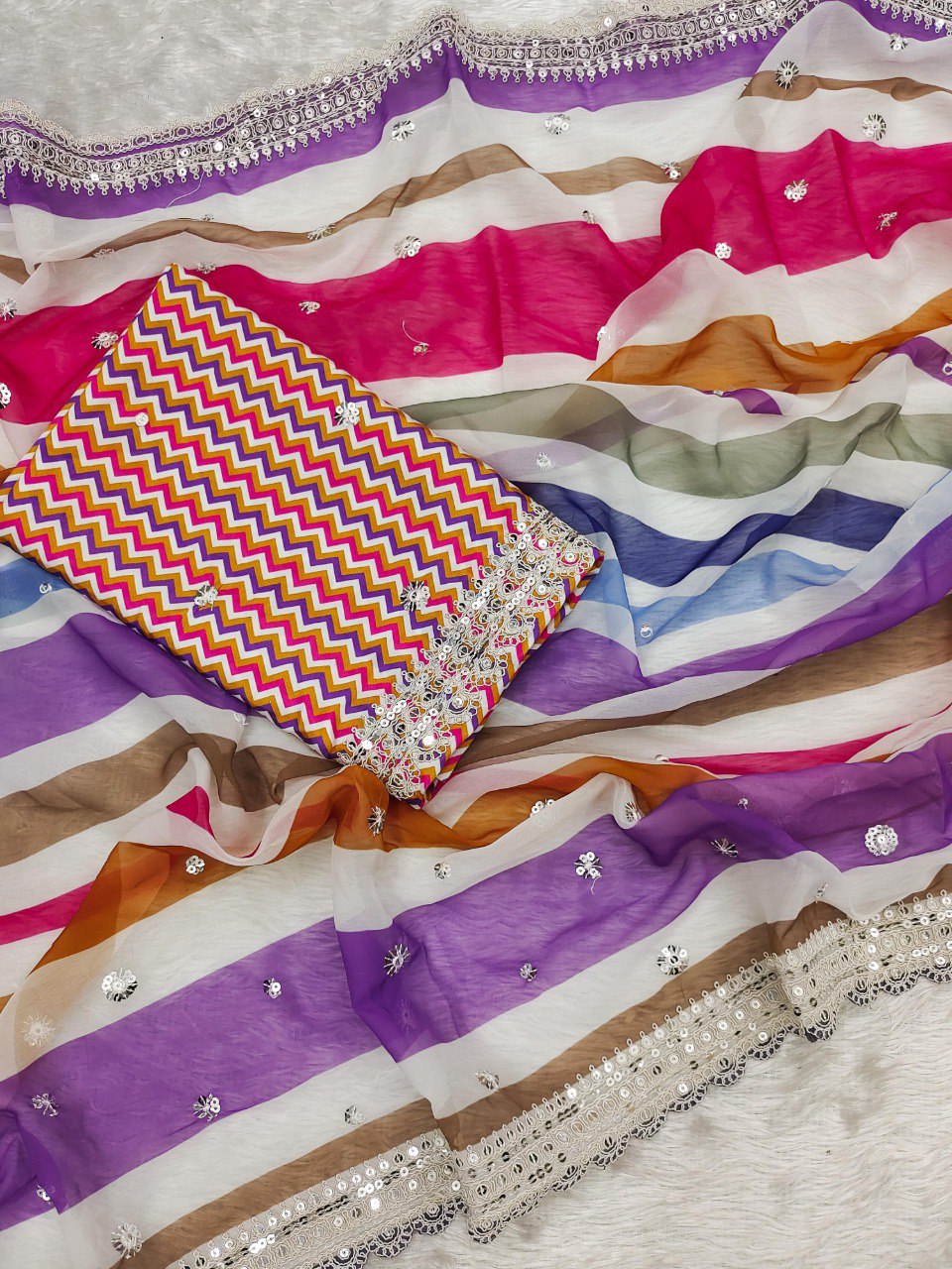 Flat lay of the pink and yellow multi-striped georgette saree fabric with the unstitched colorful chevron print crape silk blouse piece.
