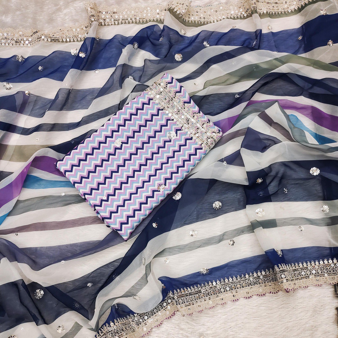 Flat lay of the blue and purple multi-striped georgette saree fabric with the unstitched blue chevron print crape silk blouse piece.