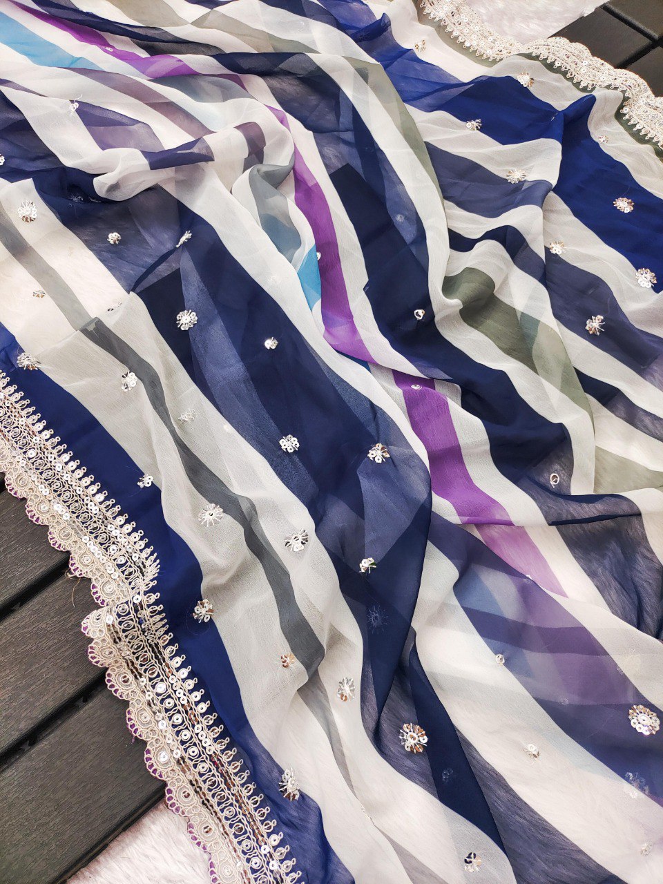 Overhead shot of the blue and purple striped georgette saree fabric, showcasing its translucent quality and sequin details.