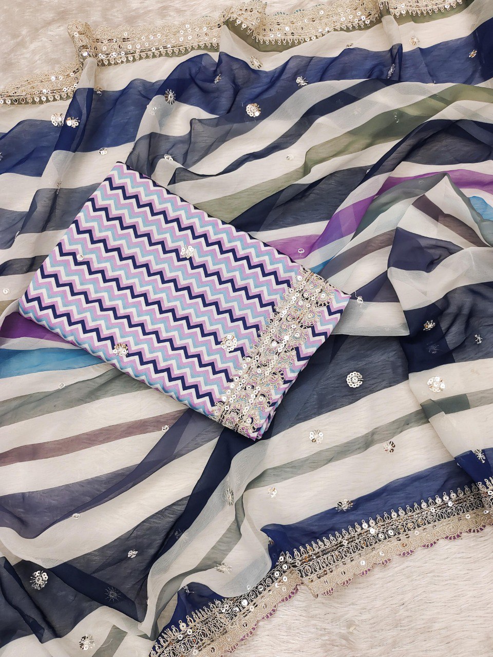 Flat lay of the blue and purple multi-striped georgette saree with the matching unstitched chevron print blouse piece.
