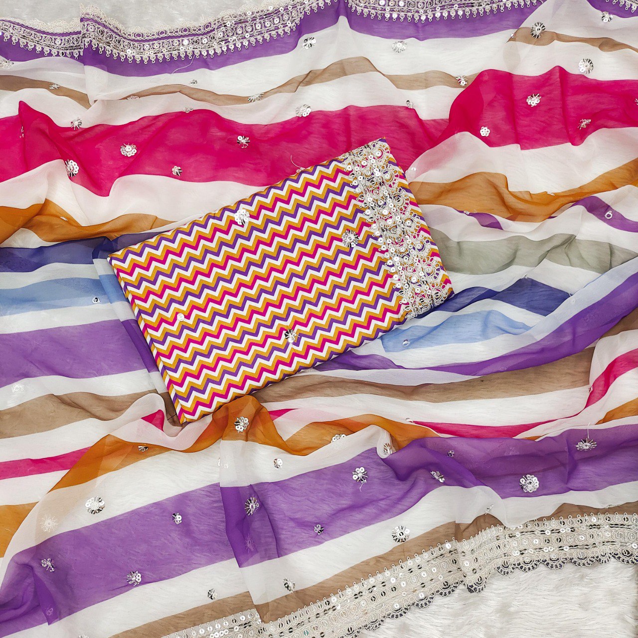 Flat lay of the pink and yellow multi-striped georgette saree with the matching unstitched chevron print blouse piece.