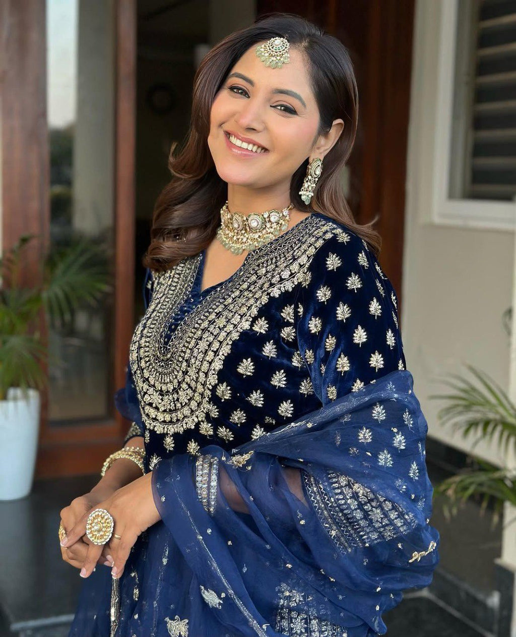 Smiling model in a stunning two-tone blue velvet kurti plazzo set with intricate gold embroidery and traditional jewelry.