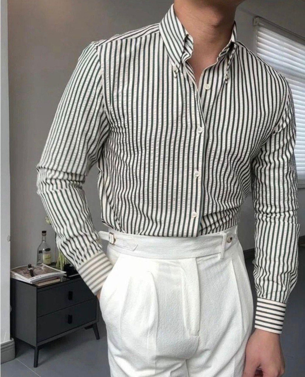 Dapper man in a green and white striped cotton shirt, untied, with white high-waisted trousers, showcasing a fresh style