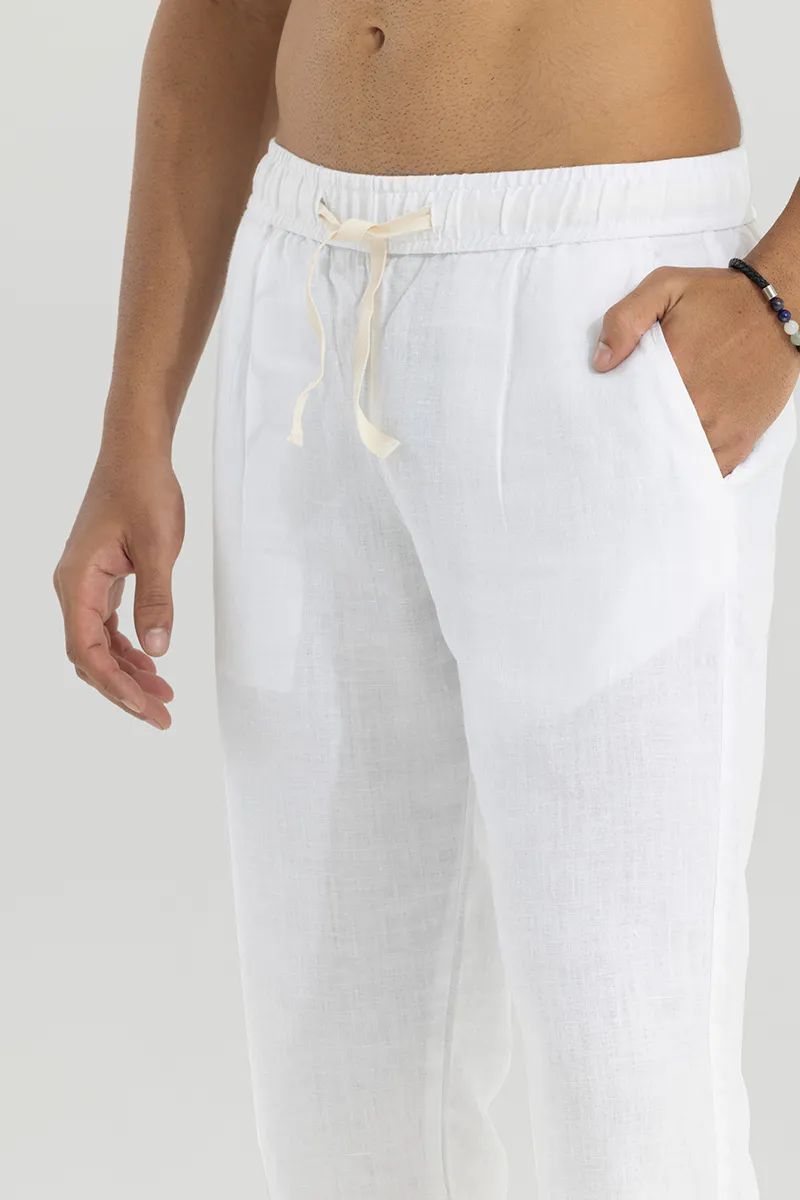 Close-up of a man's torso and legs wearing white cotton linen pants with a natural drawstring, showcasing texture and pockets.