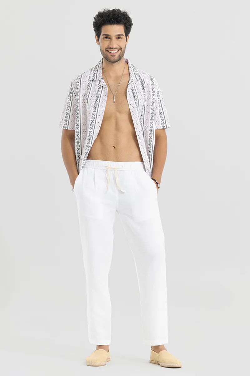 Full-body shot of a smiling man posing in white cotton linen pants and an open patterned shirt, looking stylish and relaxed.