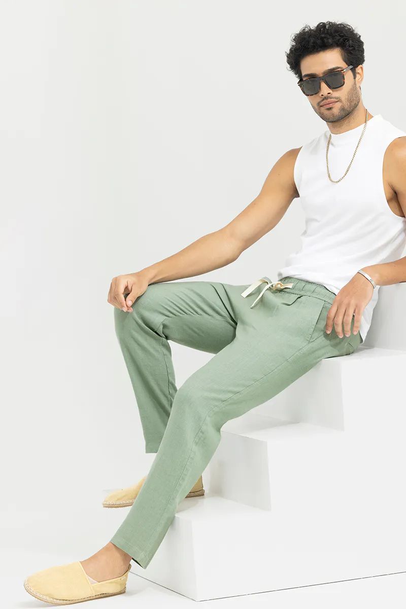 A casually posed man sitting on white steps, wearing pista green cotton linen pants and a white tank top, with sunglasses.