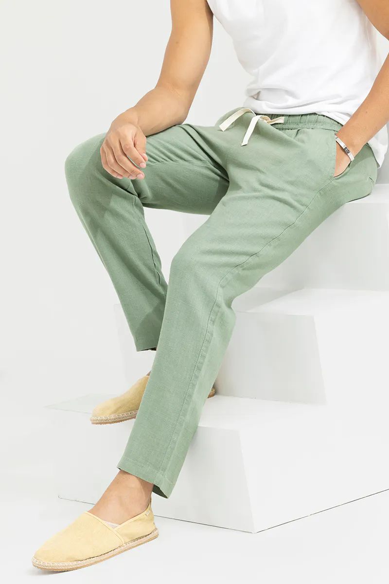 Close-up of a man sitting comfortably on stairs, highlighting the drawstring and pockets of pista green linen blend trousers.