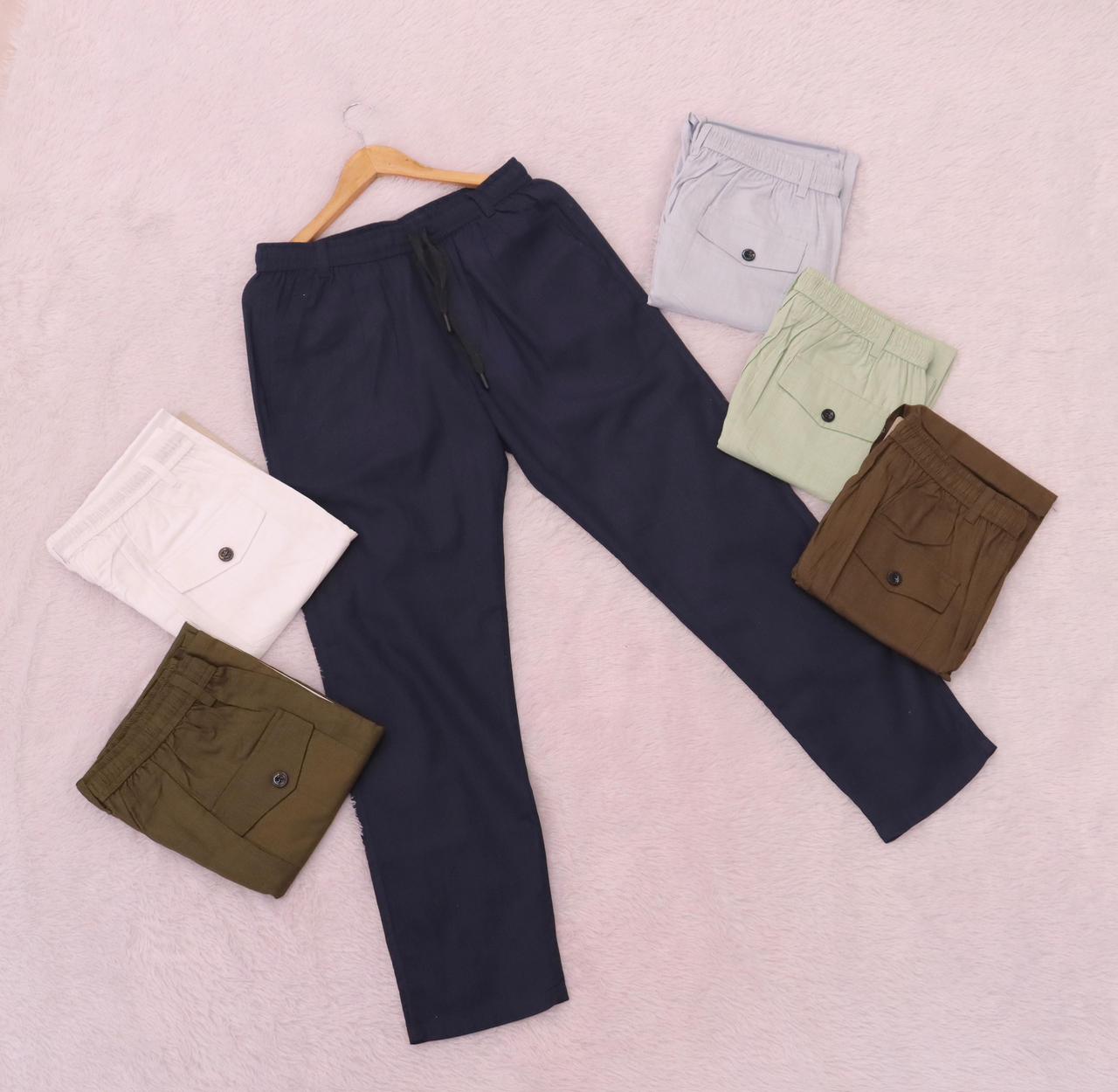 Flat lay arrangement of TRENDBUY men's cotton linen pants in multiple colors: navy, white, pista, military, mehndi, and grey, showcasing a back pocket detail.