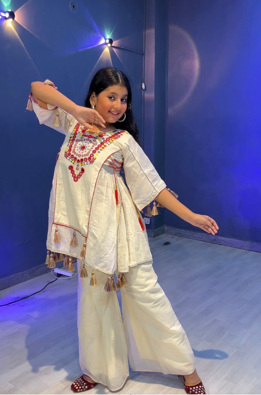 Girl in embroidered khadi cotton plazzo set, showcasing side tassel details and flowing sleeves, striking a fun pose.