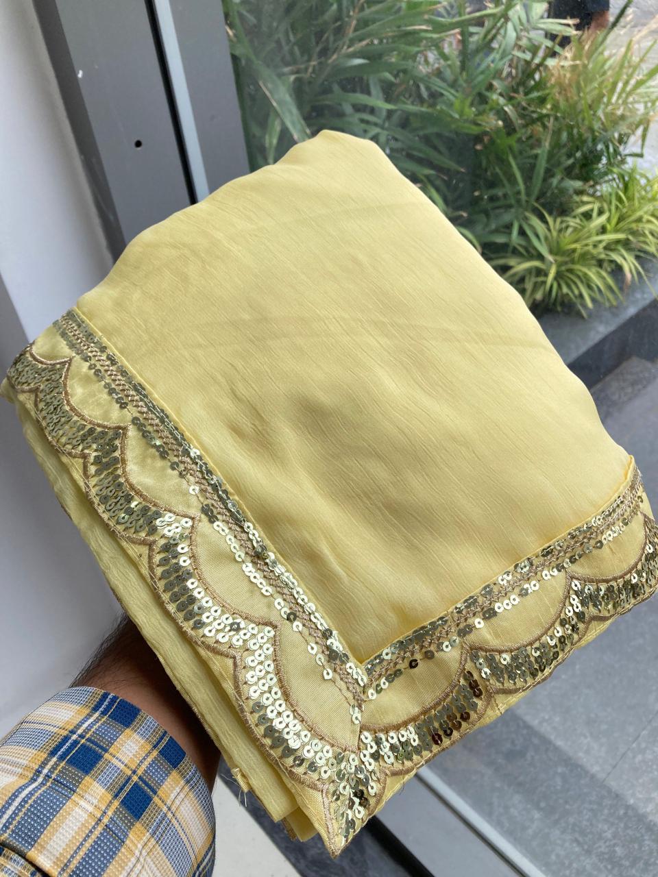 Close-up shot of the neatly folded light yellow Moss Chiffon saree, highlighting the scalloped sequin lace border being held by a hand.