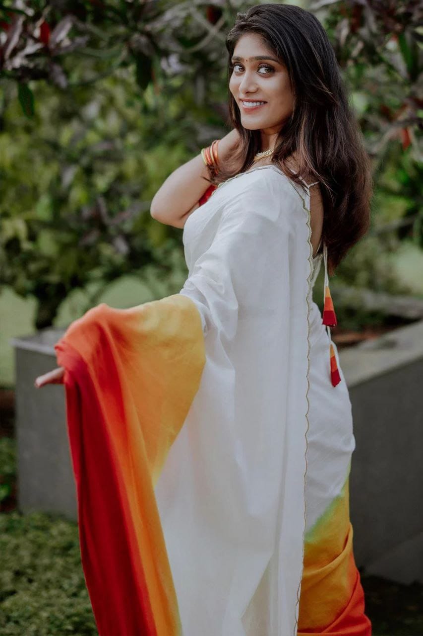 Model showcases a white linen saree with vibrant red, orange, and yellow sunset ombre pallu outdoors.