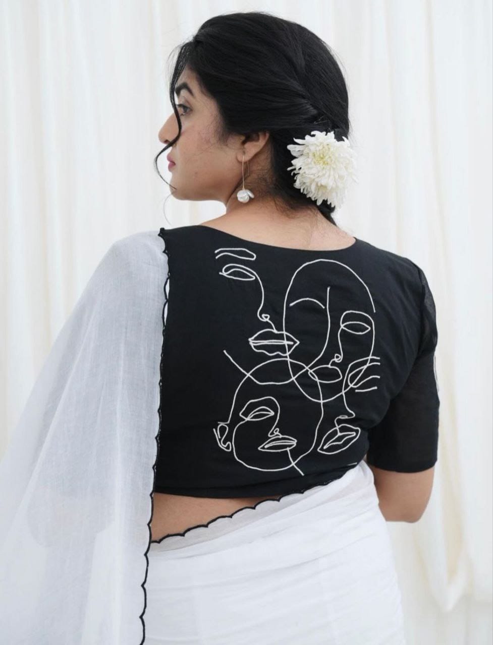 Rear view of model in a white saree, emphasizing the intricate white abstract face outlines on the black blouse.