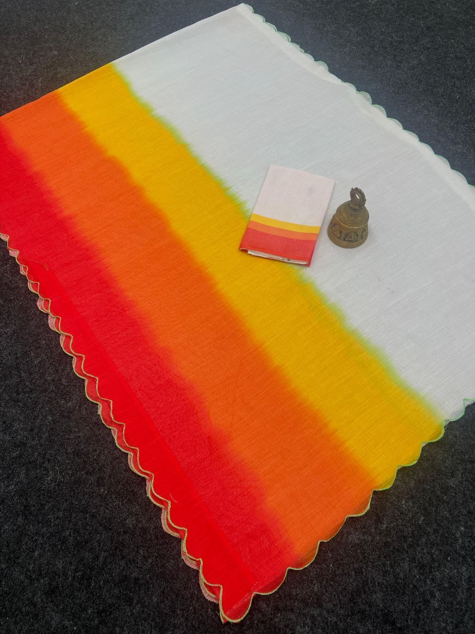 Overhead shot of a folded white and multi-color ombre linen saree with scalloped border, accompanied by matching blouse fabric.