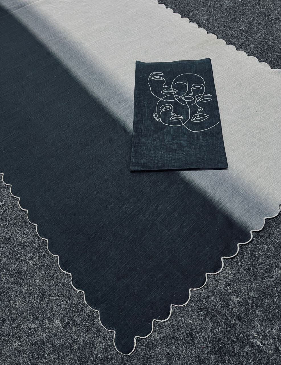 Flat lay of a black and white ombre linen saree with scalloped edges, alongside its black blouse piece featuring white abstract face prints.