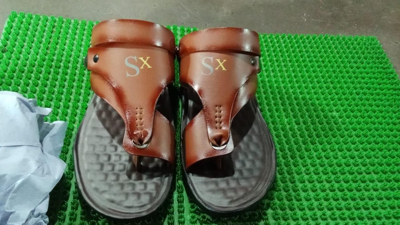 Brown sandals with 'Sx' logo on a green textured surface