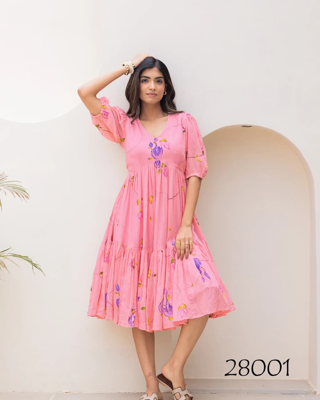 Woman wearing a pink dress with floral patterns against a white wall.