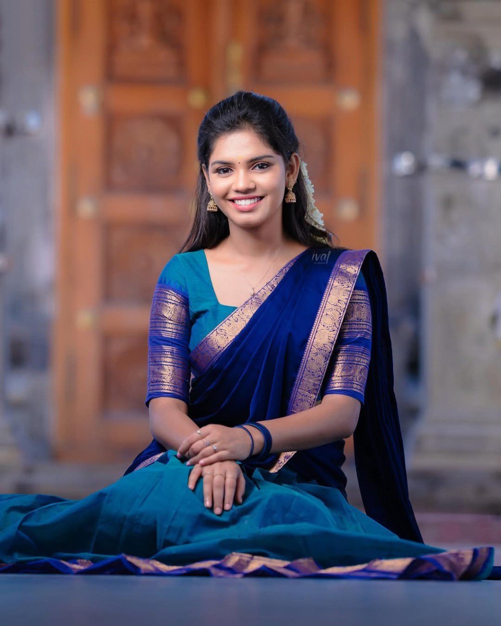 Woman in a blue saree sitting on a stone surface with a blurred background