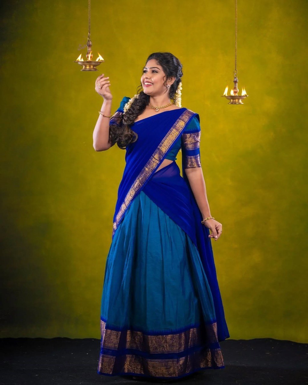 Woman wearing a blue saree with gold border against a green background