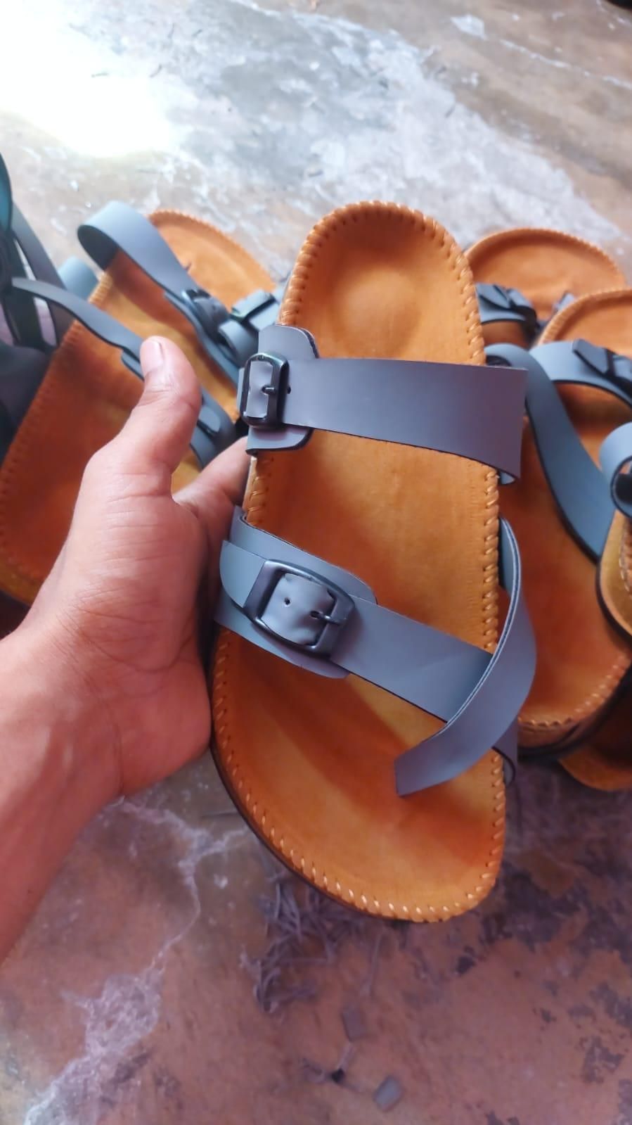 Hand holding a brown sandal with gray straps on a textured surface