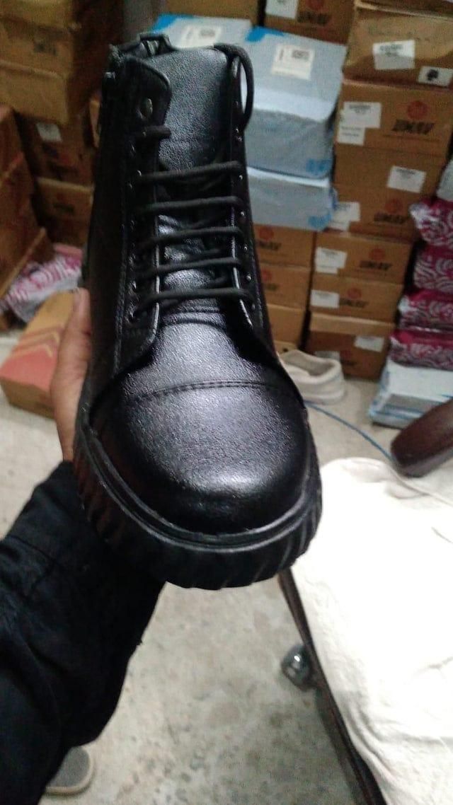 Black leather boot held in front of stacked boxes