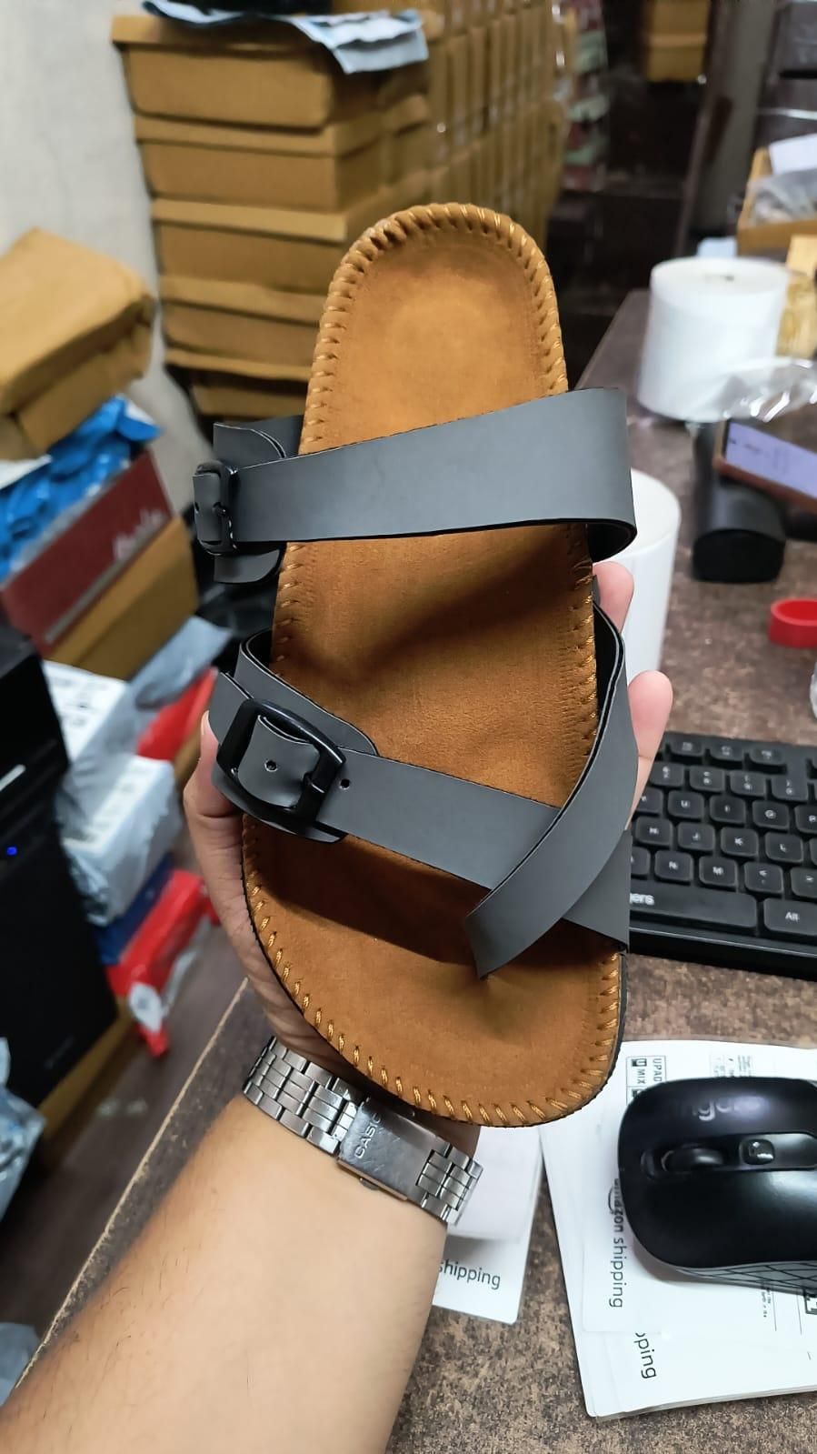 Brown sandal with a black strap held by a person in an indoor setting.
