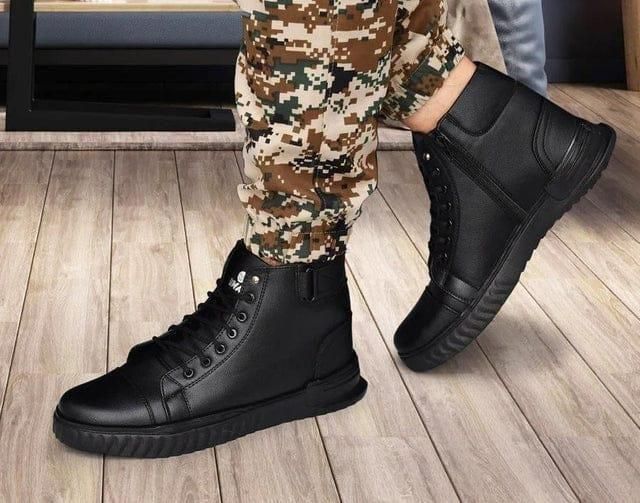 Person wearing black high-top sneakers with camouflage pants on a wooden floor.