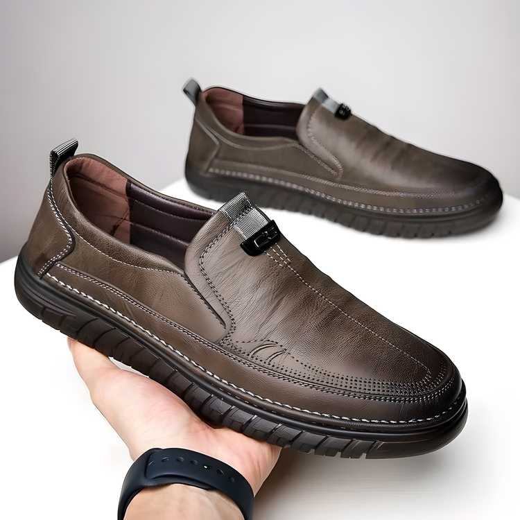 Brown leather shoes held by a hand on a light background