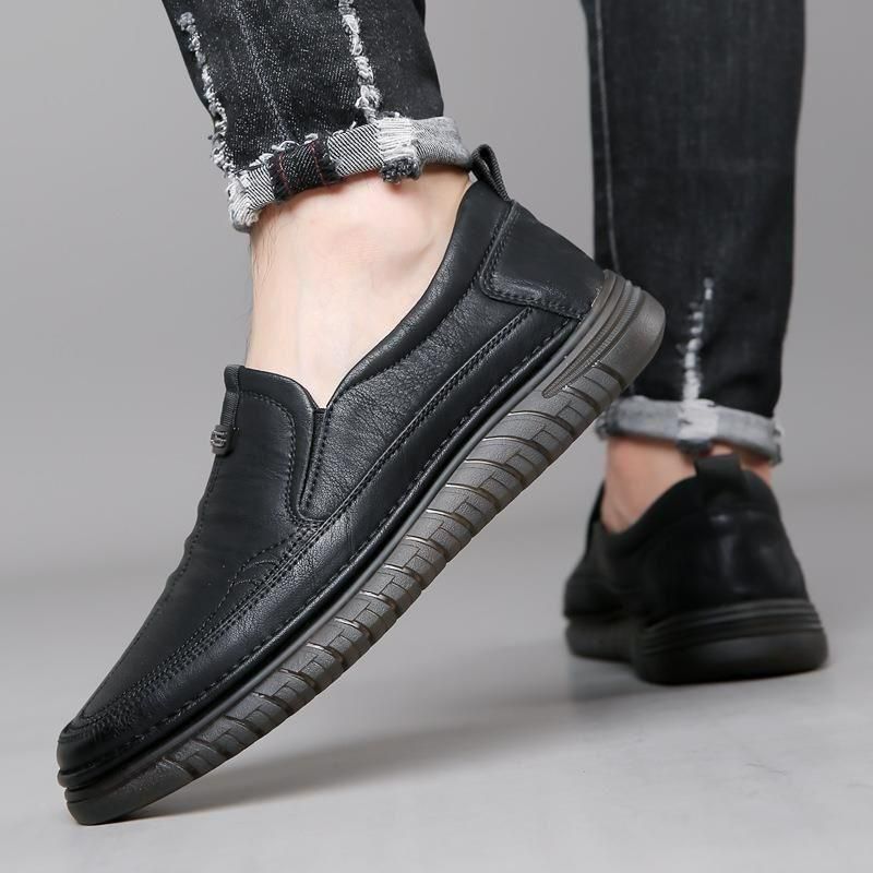 Black slip-on shoes worn with rolled-up jeans on a neutral background