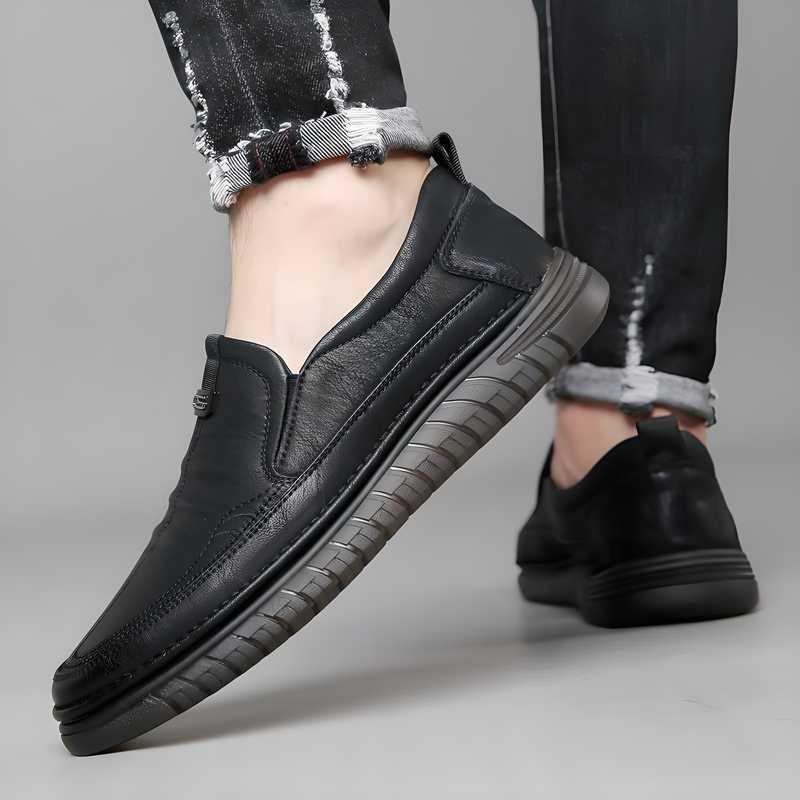 Black leather shoes worn with black pants on a neutral background